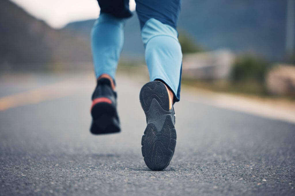 Close-up image of a person's feet running, showing they are into fitness and cardio. The setting is a long path/ road outdoors. 