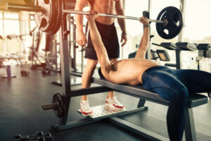 Image of model performing a fitness exercise of a bench press using modern and high quality of an Olympic bar, weight plates and a barbell rack. 